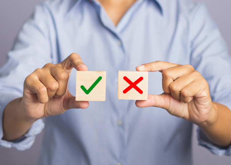Choice to accept or decline concept wrt GA consent mode v2 deadline - hand of holding two wooden cubes with a check for yes and a cross for no while standing with gray background in the studio - close up photo