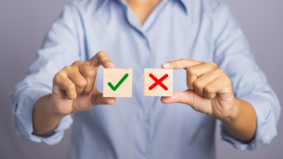 Choice to accept or decline concept wrt GA consent mode v2 deadline - hand of holding two wooden cubes with a check for yes and a cross for no while standing with gray background in the studio - close up photo